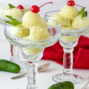Cucumber sorbet balls in margarita glass with cherry on top.