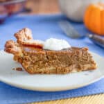 Slice of pumpkin pie on white plate with dollop of cream.