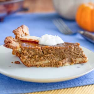 Slice of pumpkin pie on white plate with dollop of cream.
