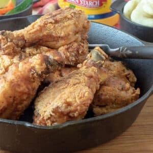Fried chicken legs in cast iron skillet.