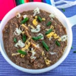 Refried beans in a white bowl garnished with chives and cheese.
