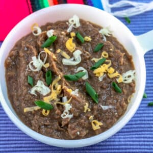 Refried beans in a white bowl garnished with chives and cheese.