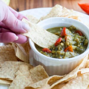 Woman's hand scooping green tomato salsa onto tortilla chip.