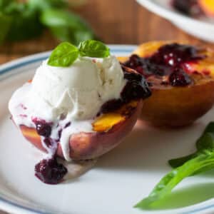 Ice cream topped grilled peaches with blackberry sauce.