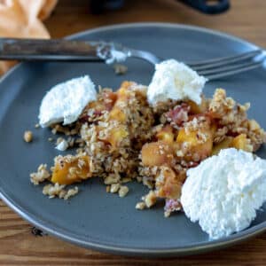 Peach crisp topped with cool whip on gray plate.