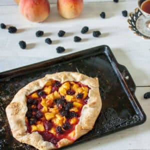 Rustic peach and blackberry galette on baking sheet.