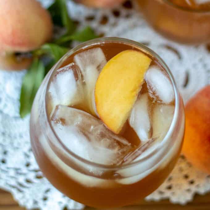Close up in peach tea in glass with peach slices garnish.