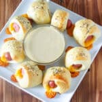 Pigs in a blanket with honey mustard dipping sauce on square white plate.