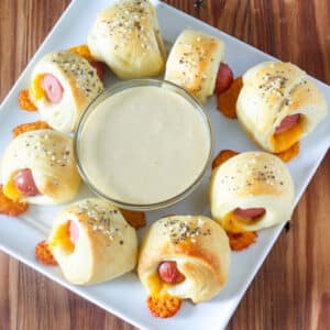 Pigs in a blanket with honey mustard dipping sauce on square white plate.