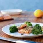Salmon topped with pesto on white plate with broccoli.