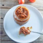 Open jar of salsa on white plate.