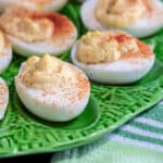 Deviled eggs topped with smoked paprika on green tray.