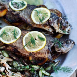 Two whole trout on pewter platter with sliced lemons.