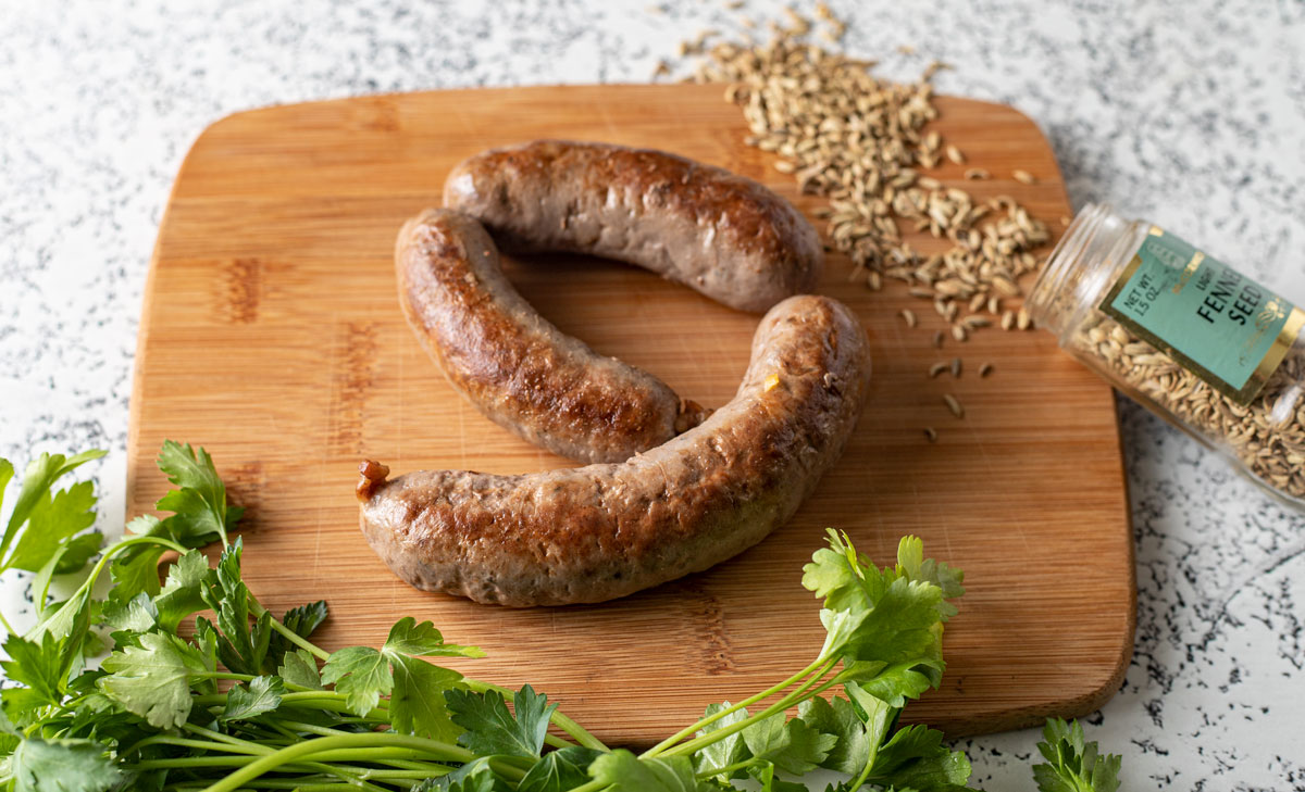 Fried venison Italian sausage with garnishes on a wooden board.