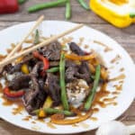 Venison teriyaki with colorful vegetables on white plate.