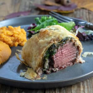 Venison Wellington on gray plate with sides.