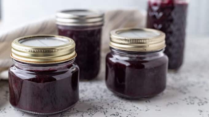 Jars of blueberry jam on white board.