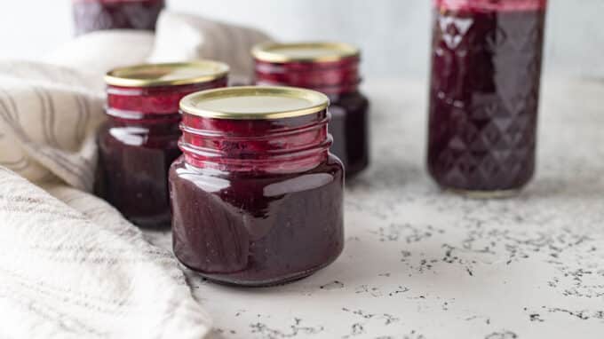 Jars of blueberry syrup on white board.