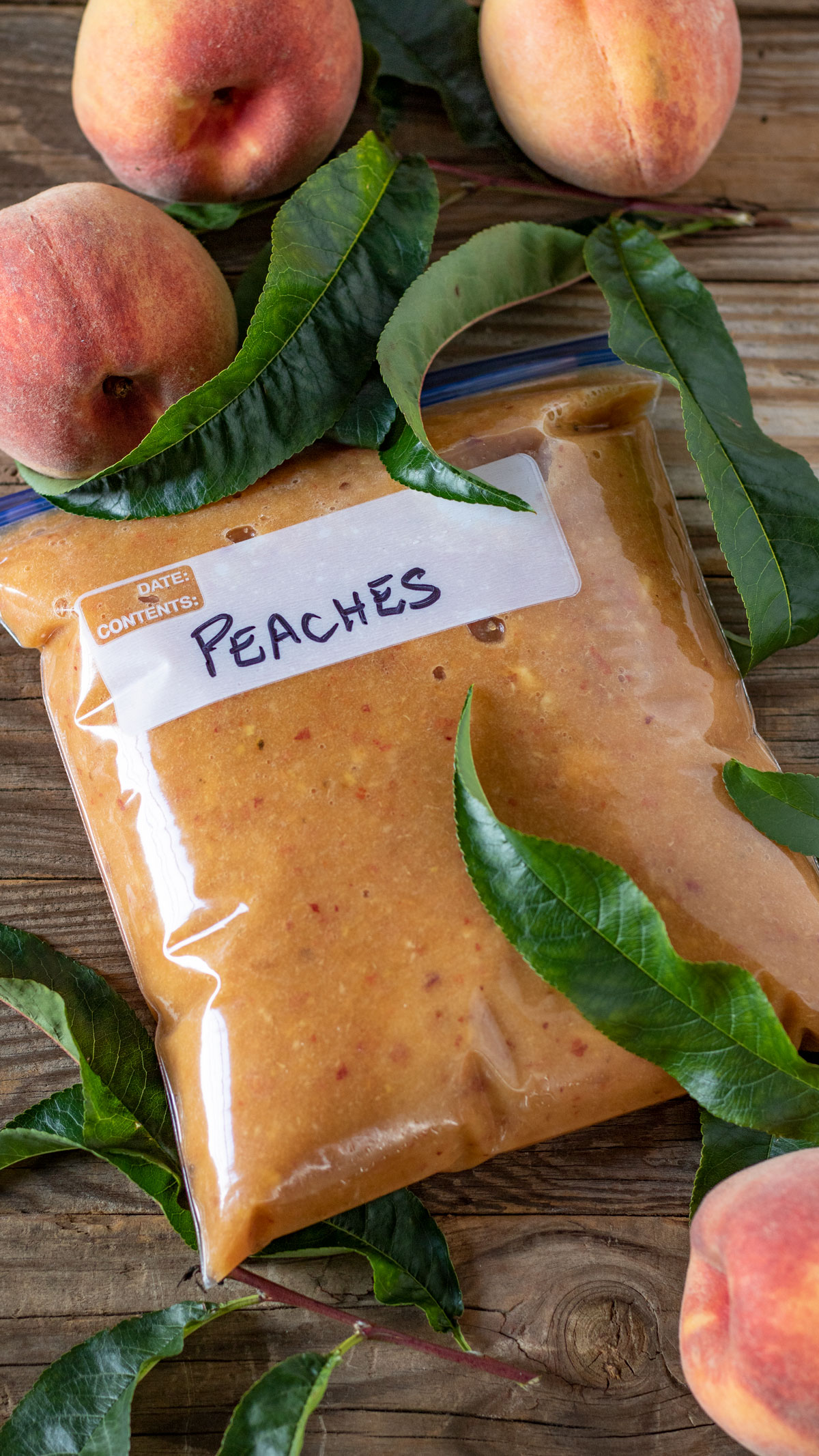 Peaches in freezer bag with peaches and peach leaves on the side.