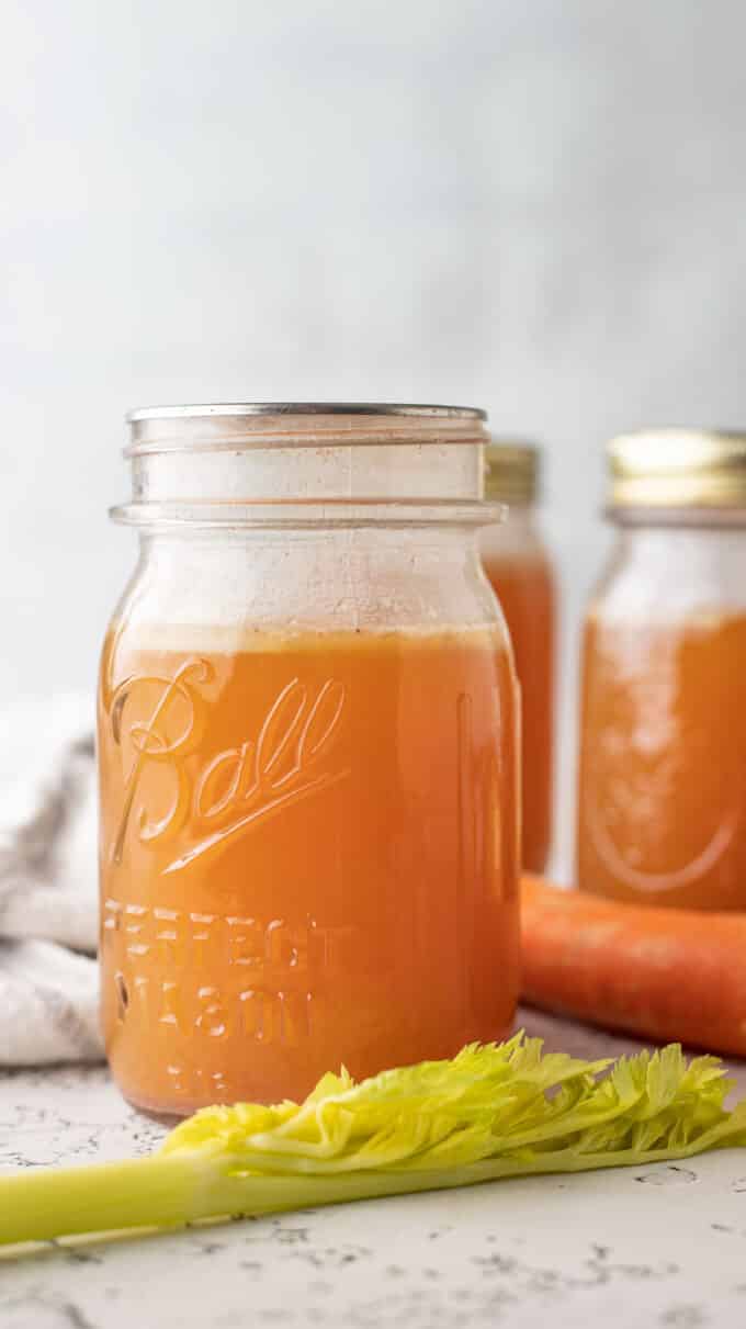 Bone broth in jars with celery and carrot garnish.