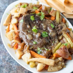 Whole venison roast with vegetables on white platter.