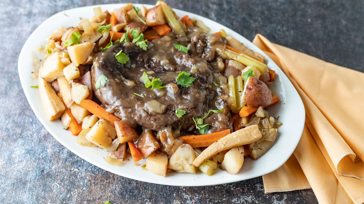 Whole roast on white platter with vegetables.