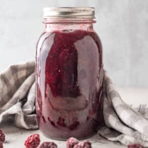 Jar of blackberry pie filling with gray checked towel.