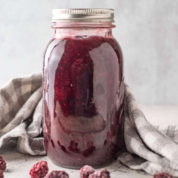 Jar of blackberry pie filling with gray checked towel.