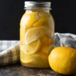 Jar of fermented lemons with a fresh lemon.