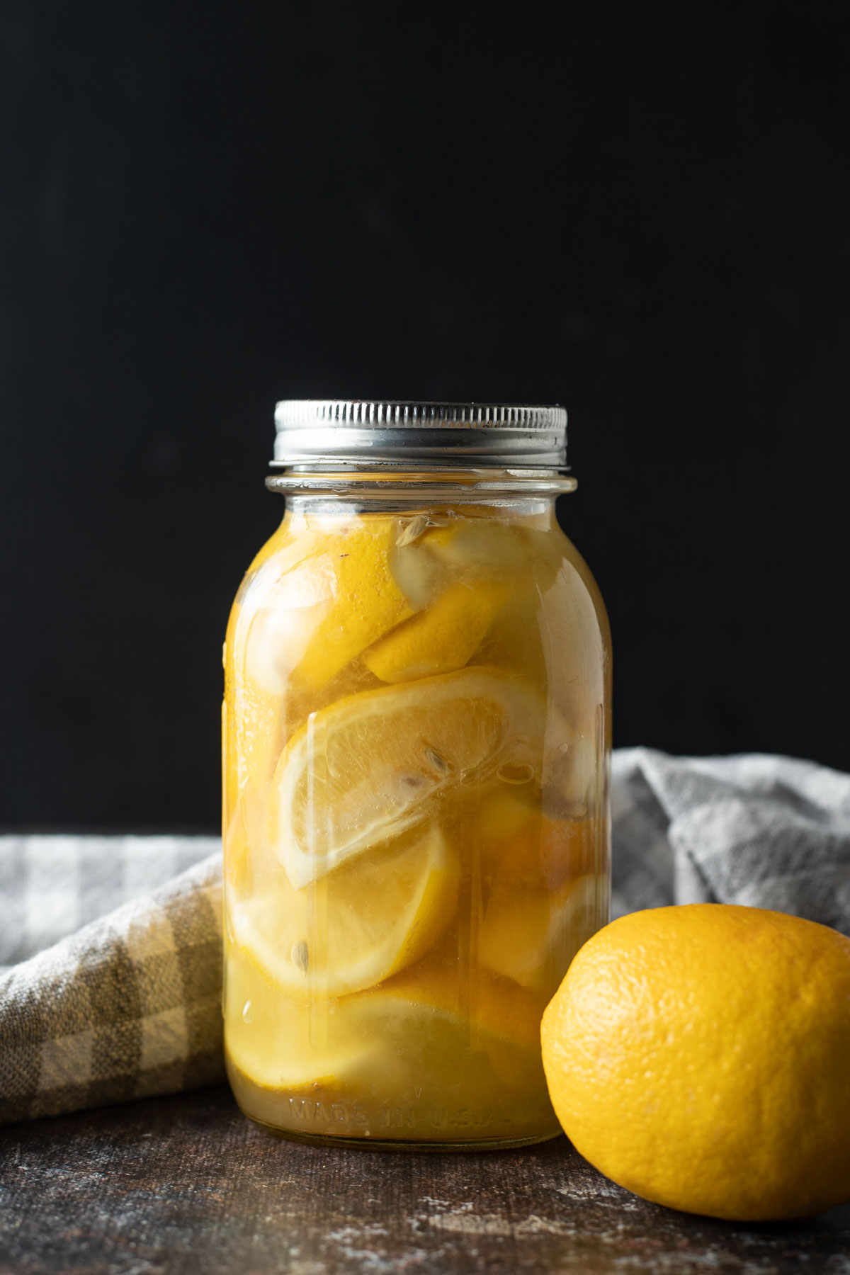 Jar of lemons with fresh lemon and gray checked tea towel.