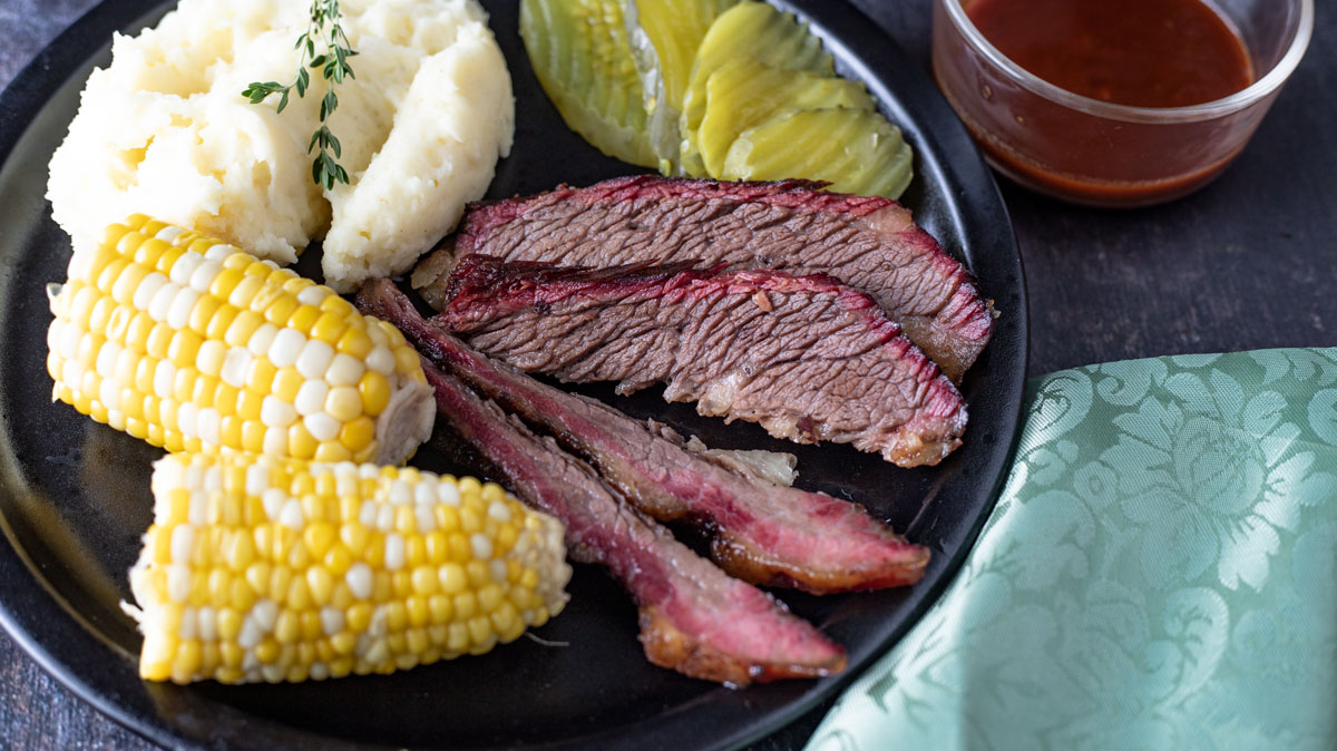 Sliced brisket and side dishes on black plate.