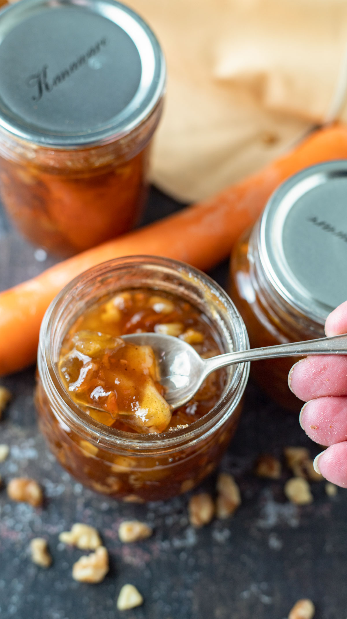 Woman's hand spooning out carrot cake jam from jar.
