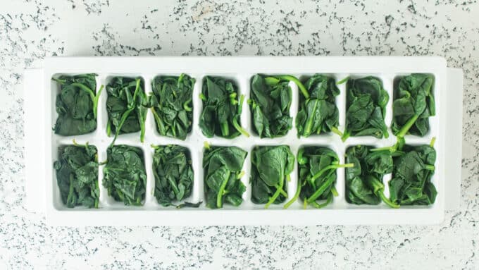 Ice cube tray filling with blanched spinach ready to freeze.