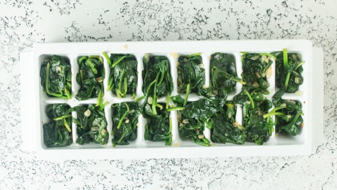 Ice cube tray filling with sautéed spinach ready to freeze.