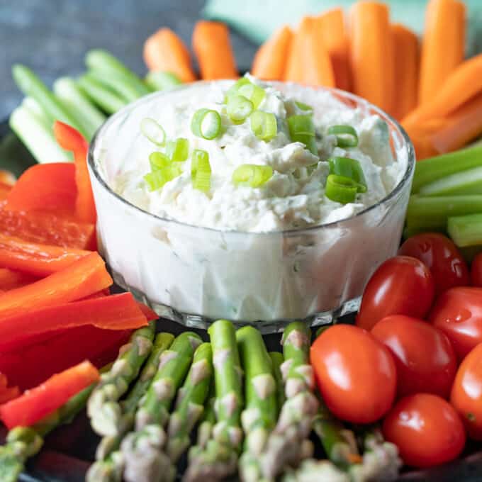 Shrimp crab dip in a bowl with colorful veggies around it.