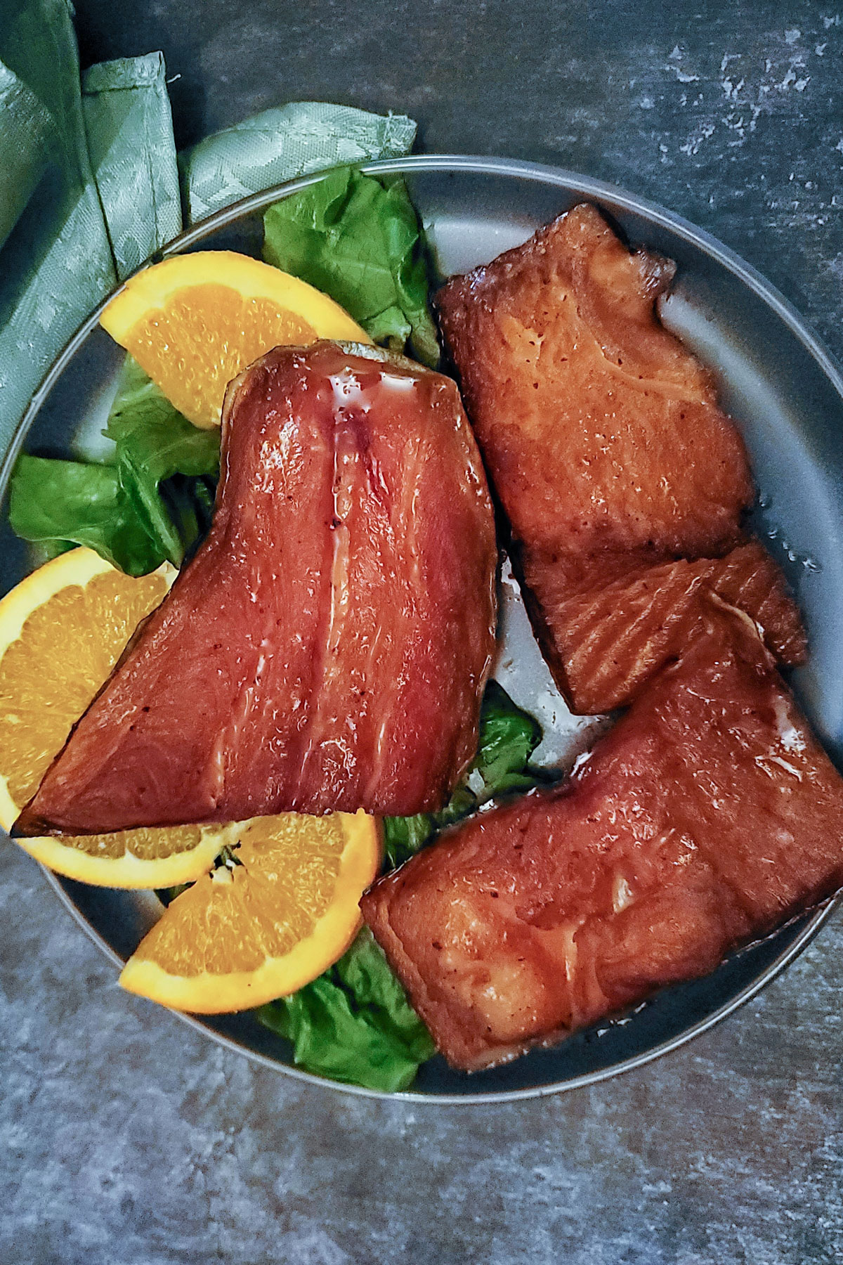 Glistening pieces of trout on gray plate with orange garnish.