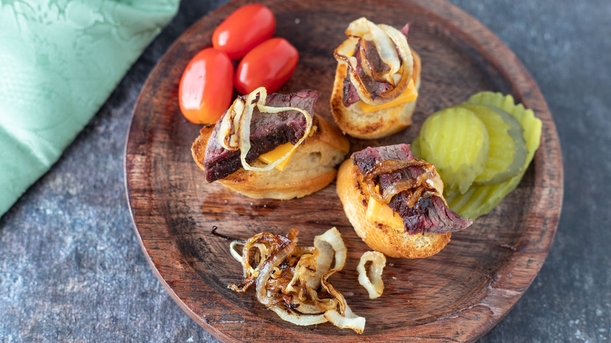 Appetizer plate with brisket crostini and cherry tomatoes and pickle slices.