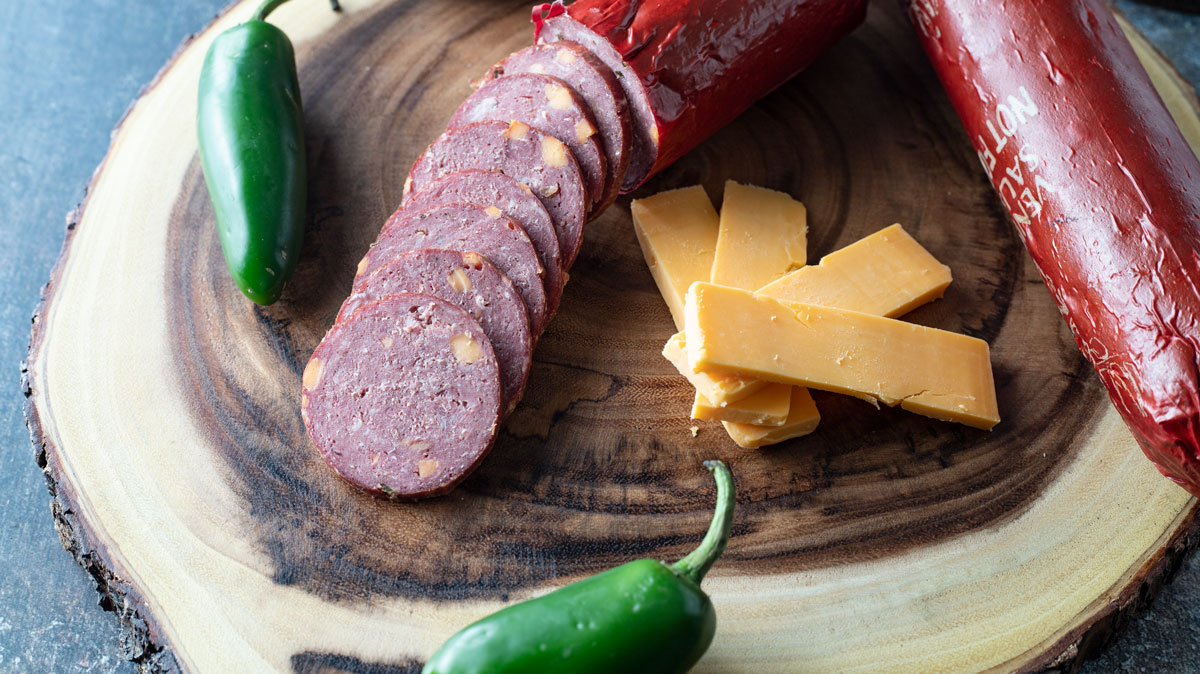 Whole and sliced summer sausage on board.