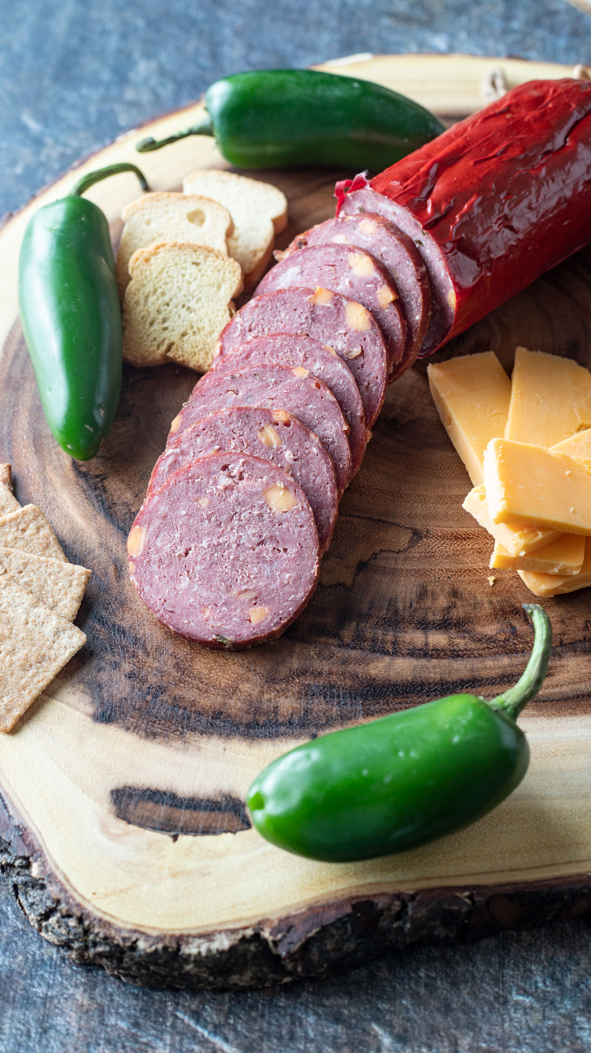 Sliced sausage on a wooden slab with crackers.