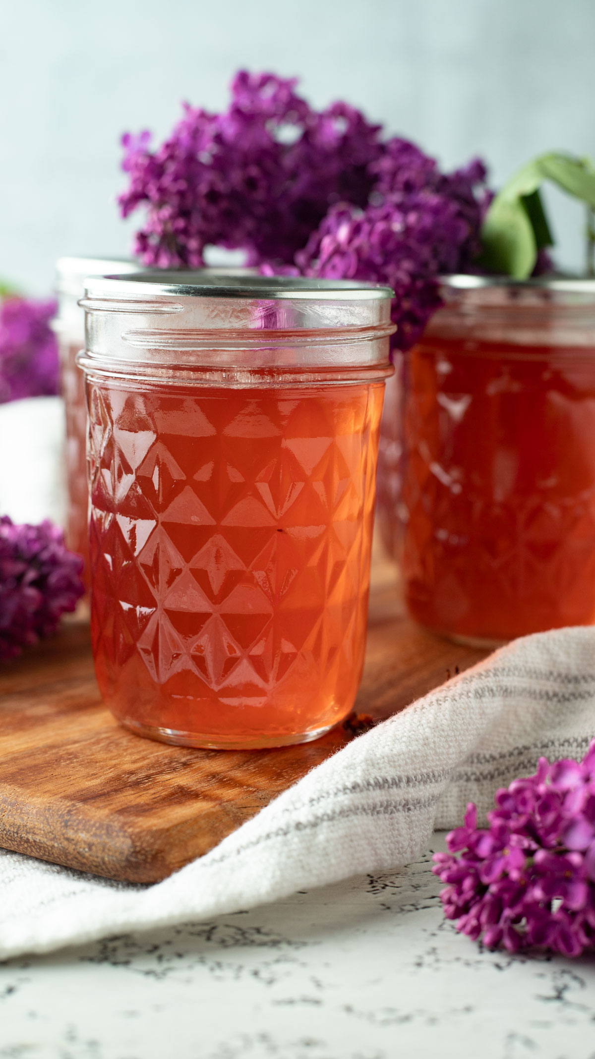 Jars of lilac jelly on a wooden cutting board.