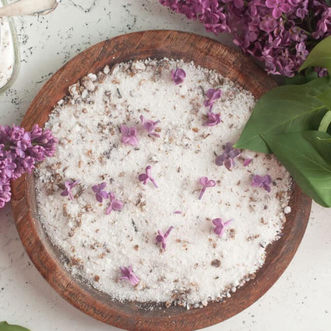 Lilac sugar on round wooden plate with lilac blooms.