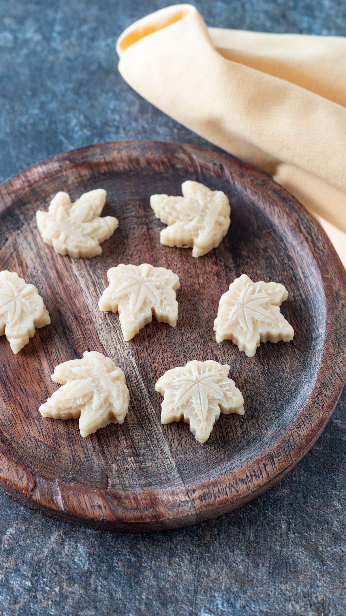 Maple leaf shaped maple candy on round wooden plate.