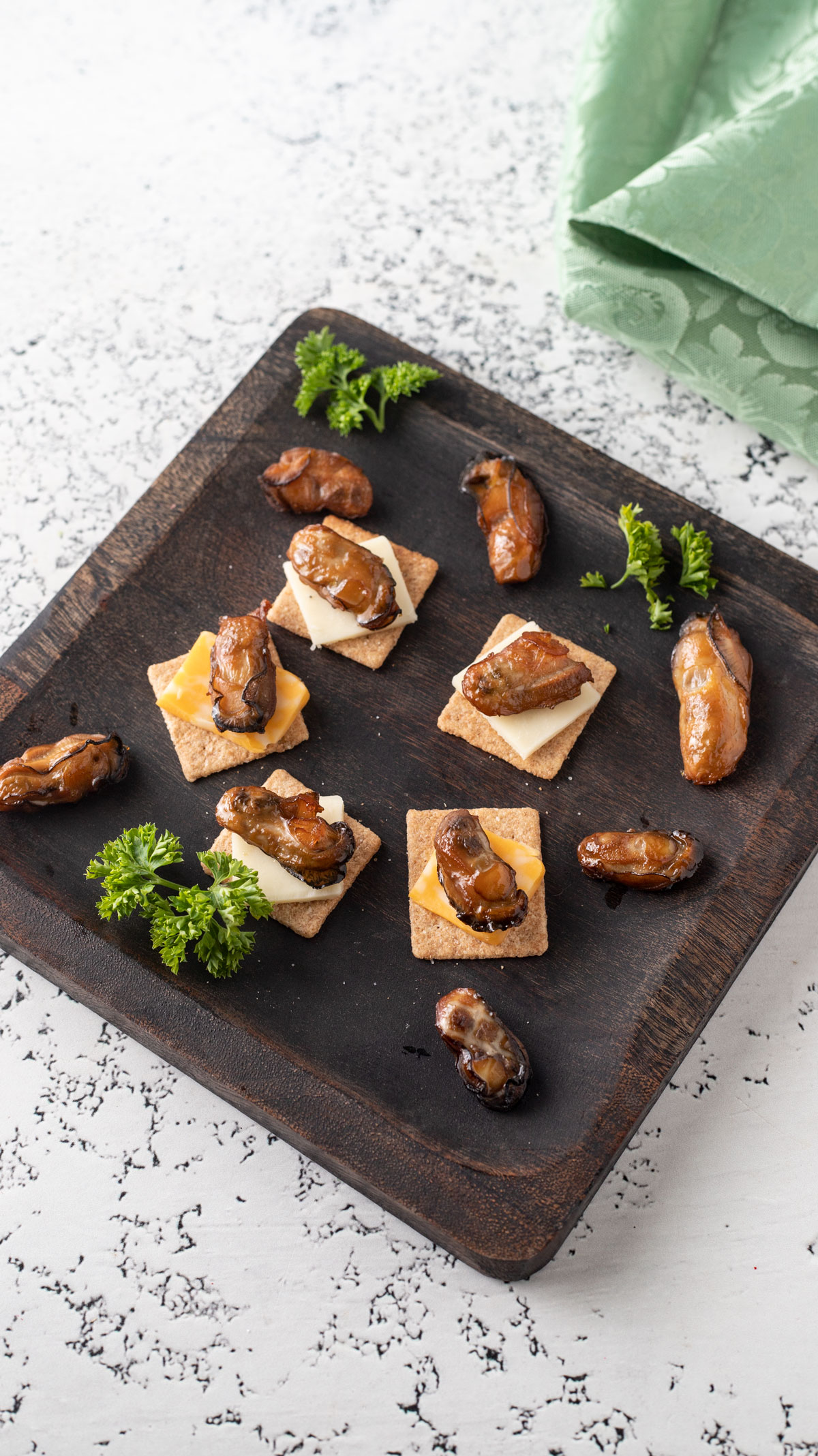 Crackers topped with cheese and an oyster on wooden plate.