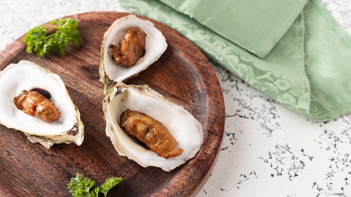 Oysters placed back in the shell on a round wooden plate.