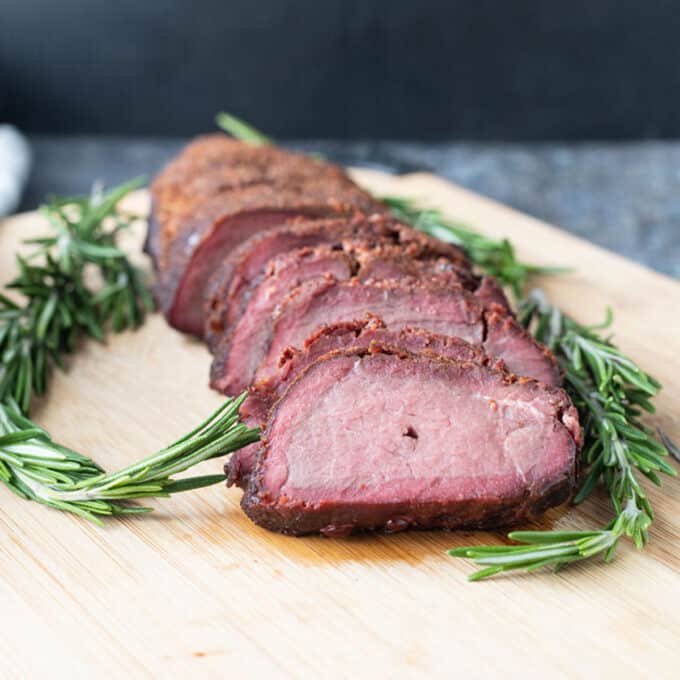 Sliced backstrap on board with fresh rosemary garnish.