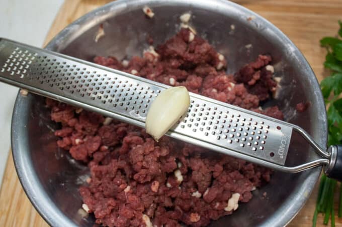 Grating garlic over meat in bowl.