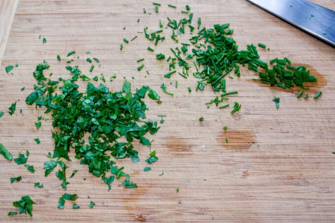 Chopped chives and parsley on cutting board.