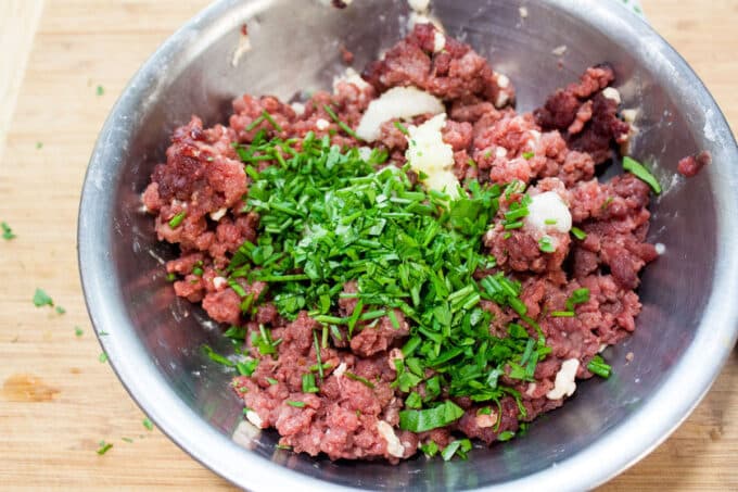Herbs added to meat in bowl.