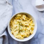 White bowl filled with chive and cheese scrambled eggs.