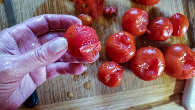 Woman's hand holding a tomato that is being peeled.